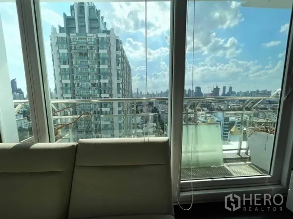 Condominium for rent or sale in Watthana, Bangkok - Balcony view of a modern high-rise and Bangkok skyline through sliding glass doors.