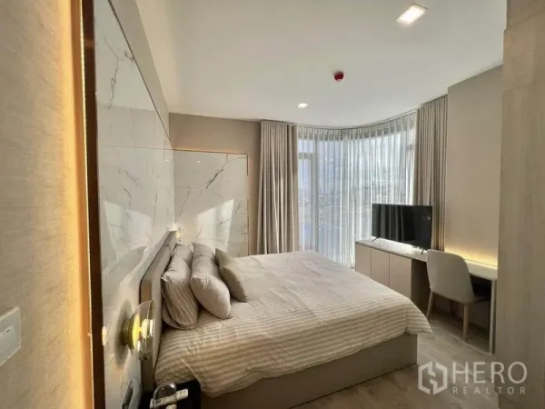 公寓 出租在Watthana, Bangkok - 明亮卧室，石纹床头墙、弧形落地帘、书桌与电视。