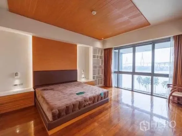 Condominium for sale in Yan Nawa, Bangkok - Primary bedroom with wood accents, king bed, built‑in storage and large windows showcasing a river and bridge view.