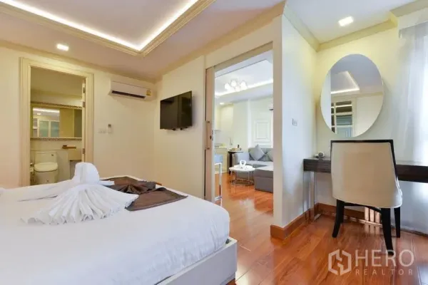 房间 出租在Khlong Toei, Bangkok - 通罗1卧公寓卧室，带电视、书桌、木地板与套卫入口。