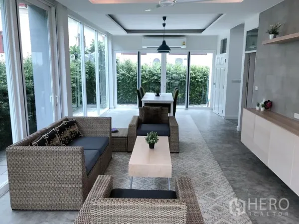 Detached House for rent or sale in Huai Khwang, Bangkok - Sunlit open-plan living and dining area with rattan sofas, full-height glass and garden views.