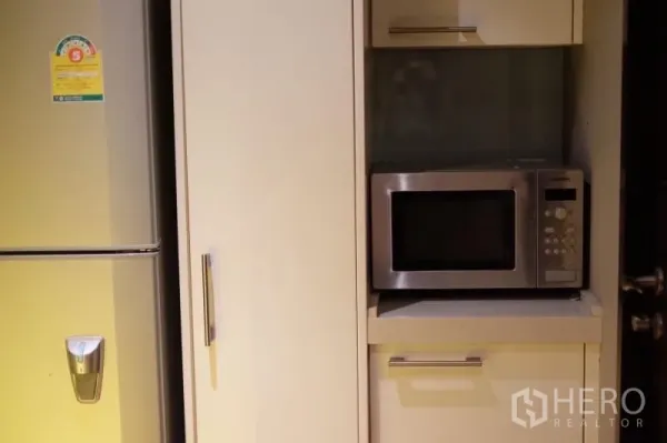 Condominium for rent in Watthana, Bangkok - Compact kitchen with stainless refrigerator and built-in microwave set in white cabinetry.
