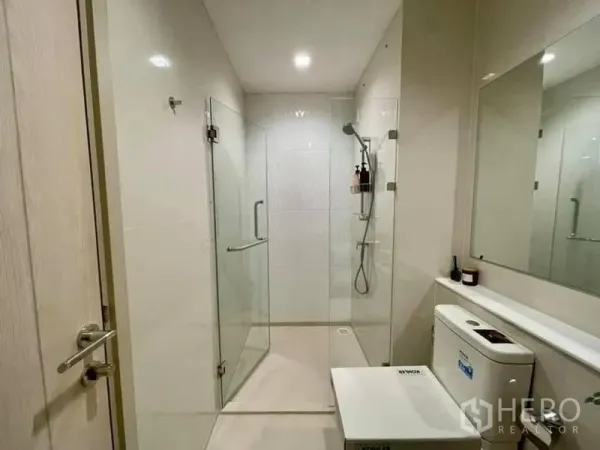 Condominium for rent in Pathum Wan, Bangkok - Glass-enclosed walk-in shower with handheld showerhead in a minimalist white-tiled bathroom.