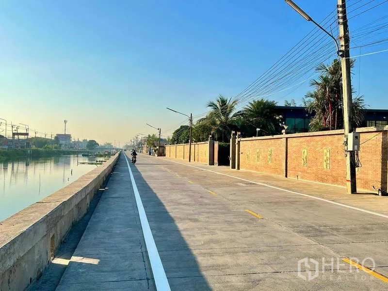 บ้าน ขายในKhlong Luang, Pathum Thani - ถนนคอนกรีตเลียบคลองขนานไปกับกำแพงอิฐยาวของตัวโครงการ