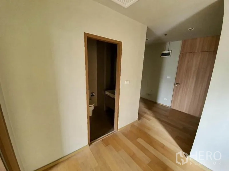 Condominium for sale in Ratchathewi, Bangkok - Bedroom entrance beside bathroom showing minimalist interior and wood flooring.