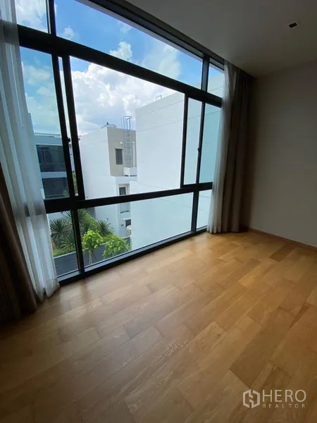 Detached House for rent in Huai Khwang, Bangkok - Bright room with expansive window overlooking modern neighboring buildings and sky.