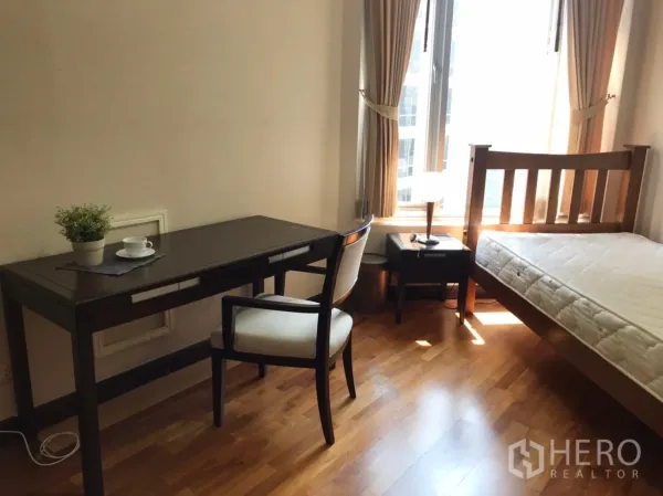 Condominium for rent or sale in Pathum Wan, Bangkok - Cozy bedroom with single bed, study desk and chair beside tall curtained windows letting in natural light.