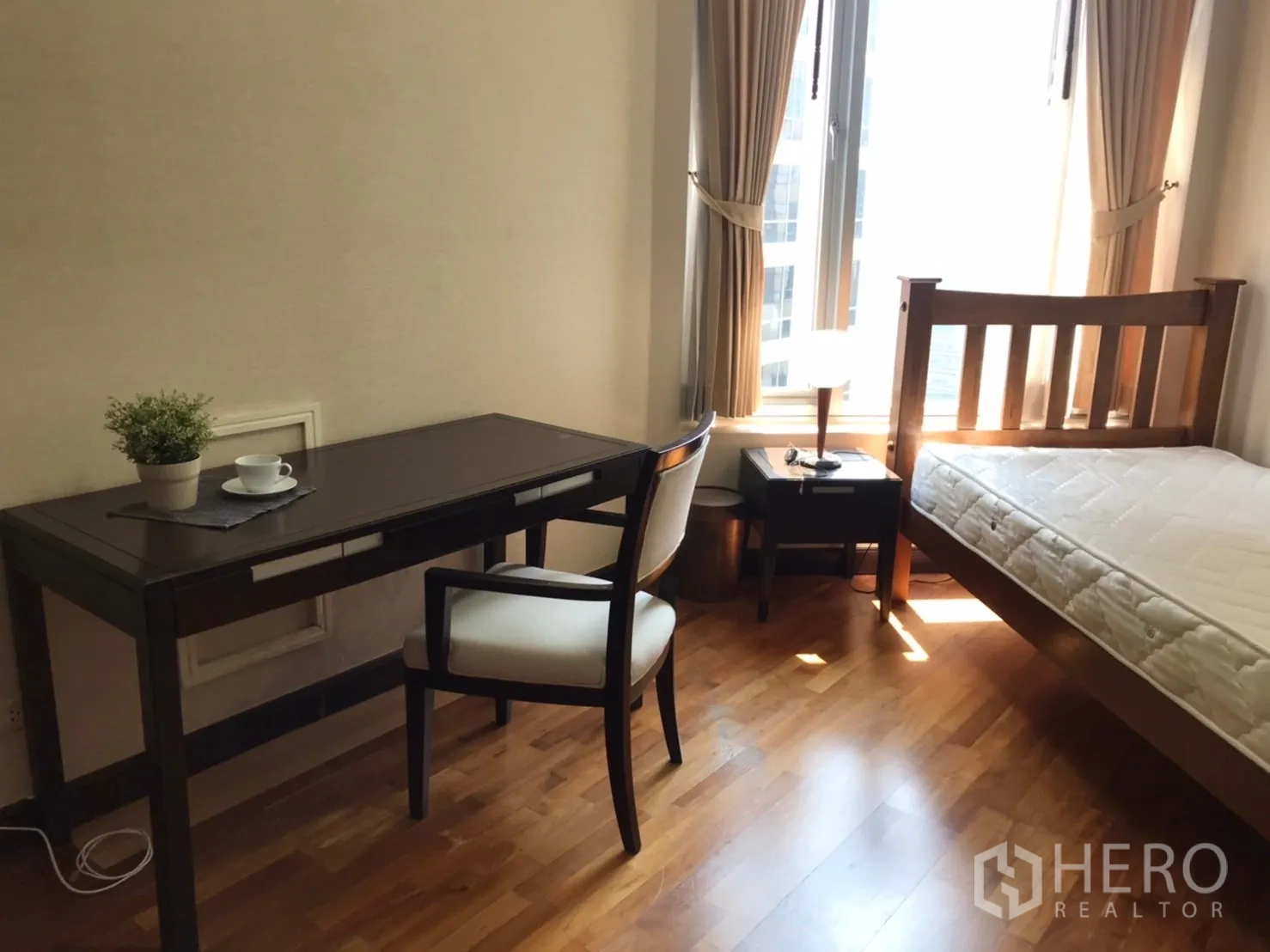 Condominium for rent or sale in Pathum Wan, Bangkok - Cozy bedroom with single bed, study desk and chair beside tall curtained windows letting in natural light.