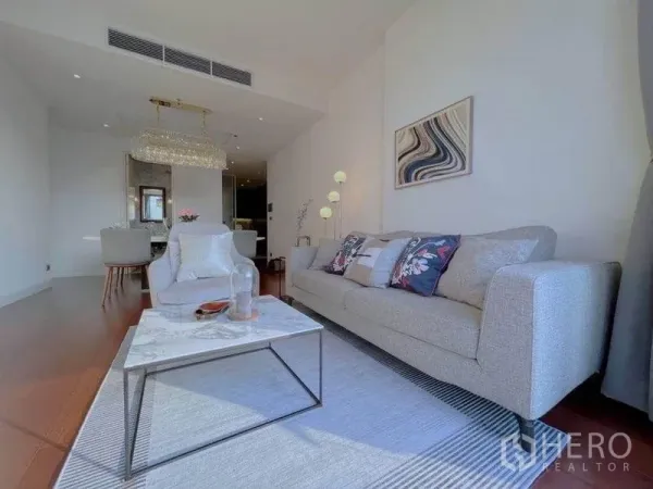 公寓 出租在Watthana, Bangkok - 明亮客厅，米色沙发、石纹茶几、木地板与水晶吊灯，连接用餐区。