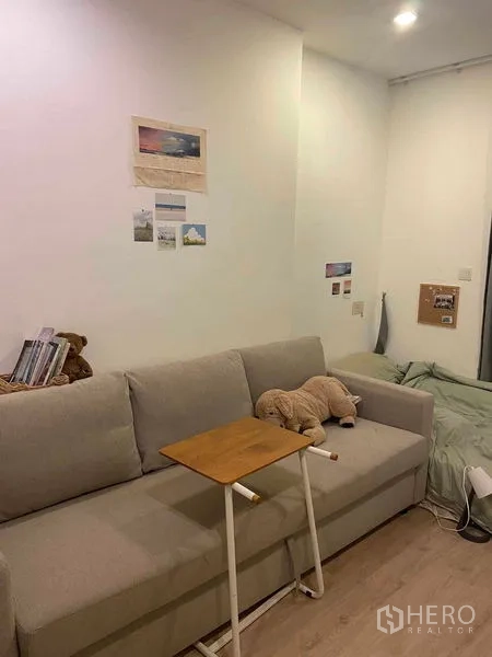 Condominium for sale in Bang Rak, Bangkok - Cozy living area with a gray sofa, small side table, wall art and wood flooring in a compact condo.