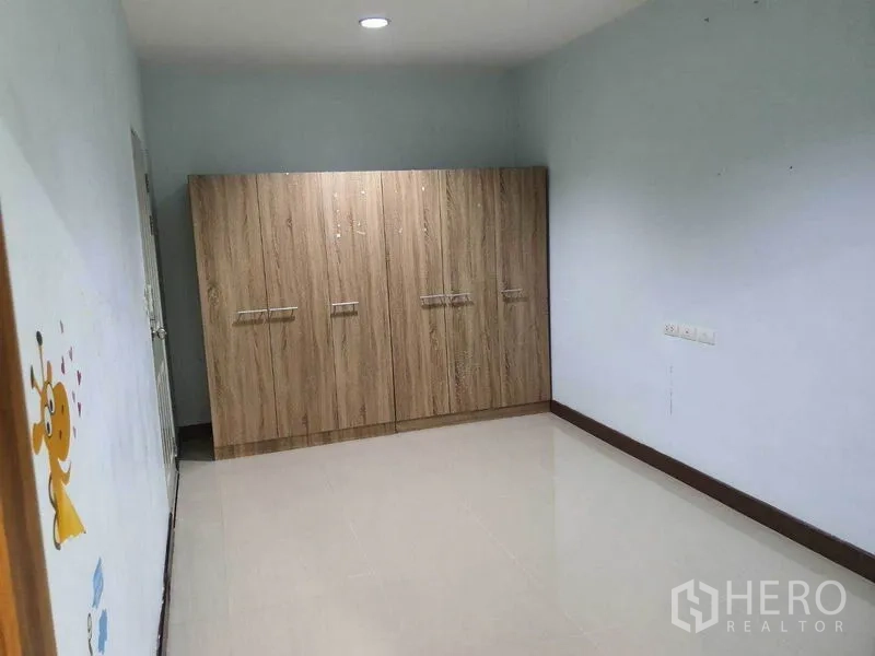 Townhouse for sale in Khlong Toei, Bangkok - Bright bedroom with a large wood wardrobe and glossy tile flooring.
