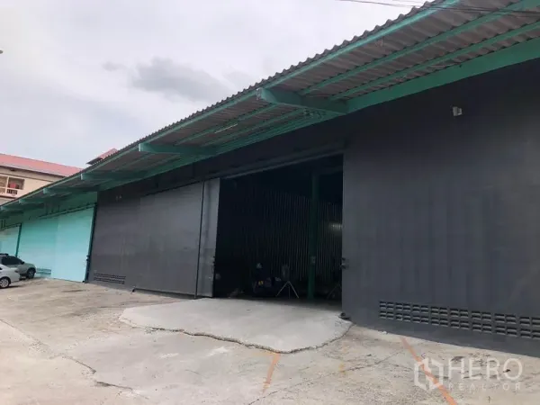 货栈 出租在Khan Na Yao, Bangkok - 仓库外立面，宽大的金属推拉门、带顶装卸区与斜坡车道。