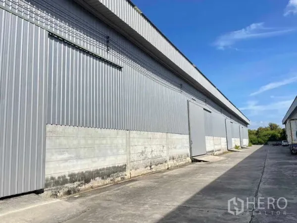 Factory for rent in Bang Pakong, Chachoengsao - Exterior of large metal-clad factory warehouse with sliding doors and a wide truck-access driveway.