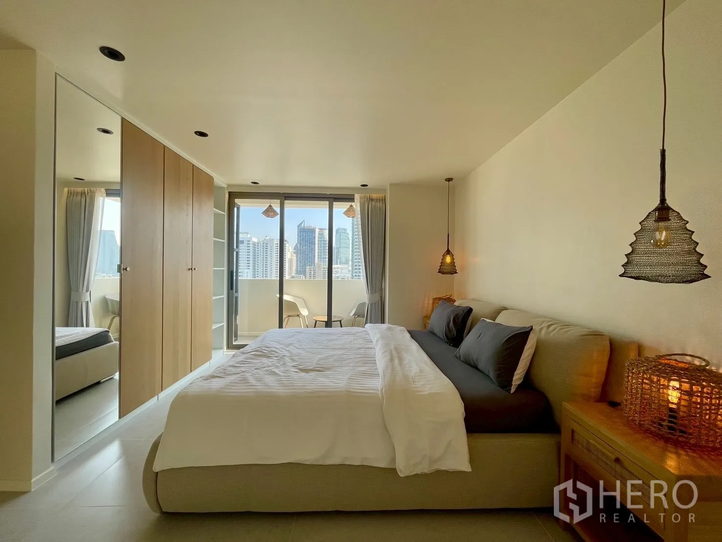 Condominium for sale in Watthana, Bangkok - Spacious bedroom with built-in wardrobes and balcony seating area beyond.