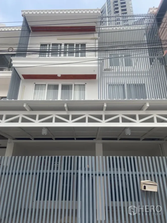 ทาวน์เฮาส์ ให้เช่าในKhlong Toei, Bangkok - ด้านหน้าทาวน์เฮ้าส์หลายชั้นสไตล์โมเดิร์น มีกันสาดซี่แนวตั้งและประตูรั้วจอดรถ.