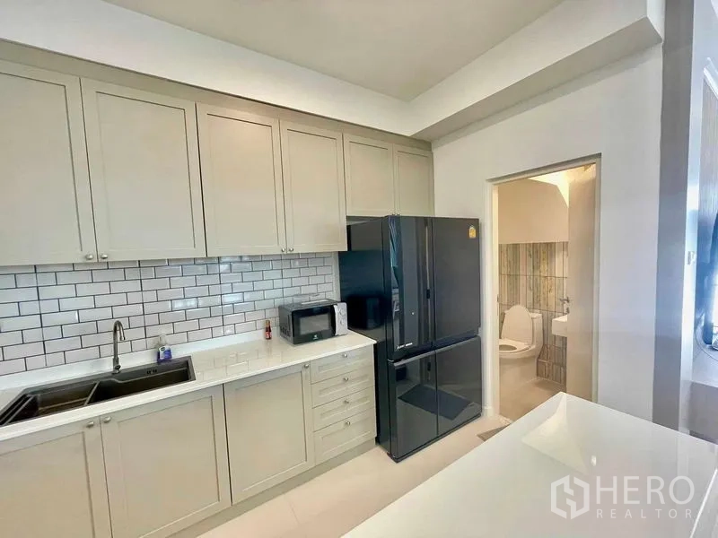 联排别墅 出租或出售在Prawet, Bangkok - 现代L型厨房，地铁砖墙面，高柜与黑色冰箱，旁边是客卫。