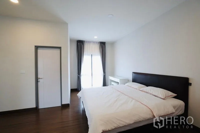 Detached House for rent in Bang Phli, Samut Prakan - Bedroom with queen bed, work desk, and balcony door with curtains.