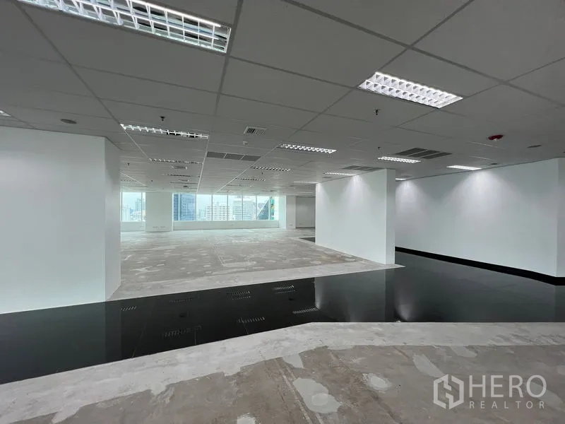 Office Space for rent - Open workspace with white walls, raised access floor section and full‑width windows facing the city.