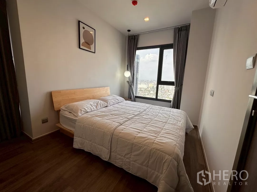 Condominium for rent in Chatuchak, Bangkok - Cozy bedroom angle with bed, curtains and skyline outlook.