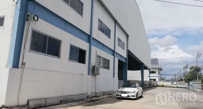 Warehouse for rent in Bang Phli, Samut Prakan - Side elevation of the warehouse and office block with driveway and parked car.