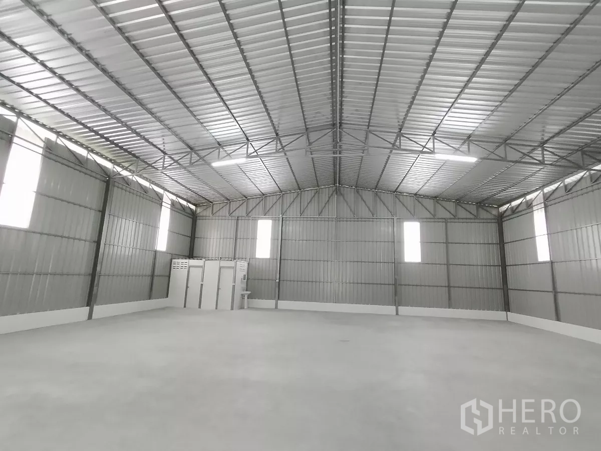 Warehouse for rent in Sai Mai, Bangkok - Spacious warehouse interior with high steel truss roof, concrete floor, and vertical skylight panels.