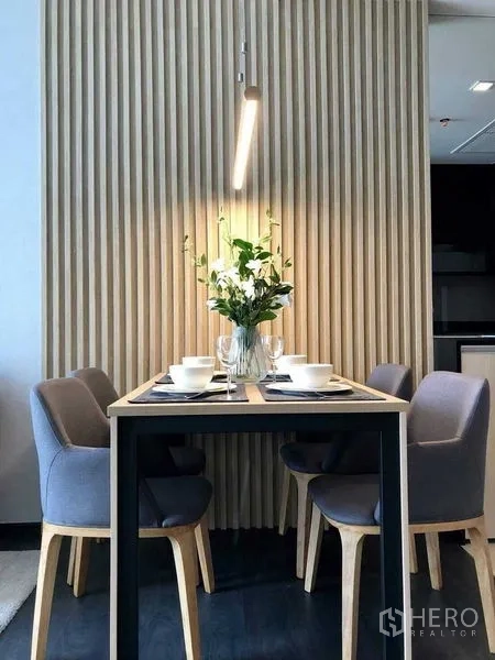 Condominium for rent in Watthana, Bangkok - Four‑seat dining set with flower centerpiece under warm pendant lighting against vertical wood panels.