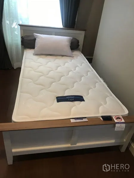 Condominium for rent or sale in Huai Khwang, Bangkok - Cozy bedroom with single bed, white frame and mattress, wood floors and curtained window in a Huai Khwang condo.