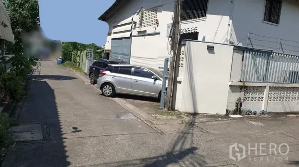 Warehouse for rent in Suan Luang, Bangkok - Narrow lane with cars parked beside a gated warehouse exterior in Suan Luang.