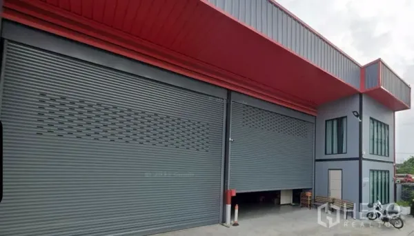 Warehouse for rent in Bang Kapi, Bangkok - Close view of gray rolling doors under a red canopy with a glass corner office at a Bangkok warehouse.
