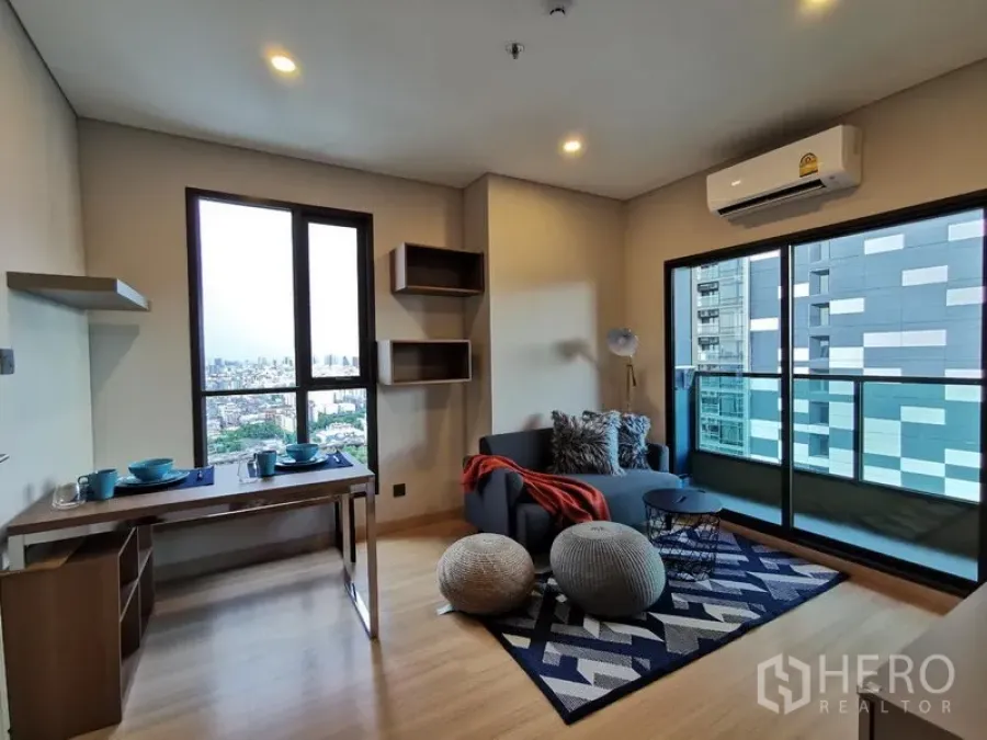 Condominium for rent in Ratchathewi, Bangkok - Open-plan living room with sofa, dining/work table, and balcony via sliding glass doors offering Bangkok skyline views.