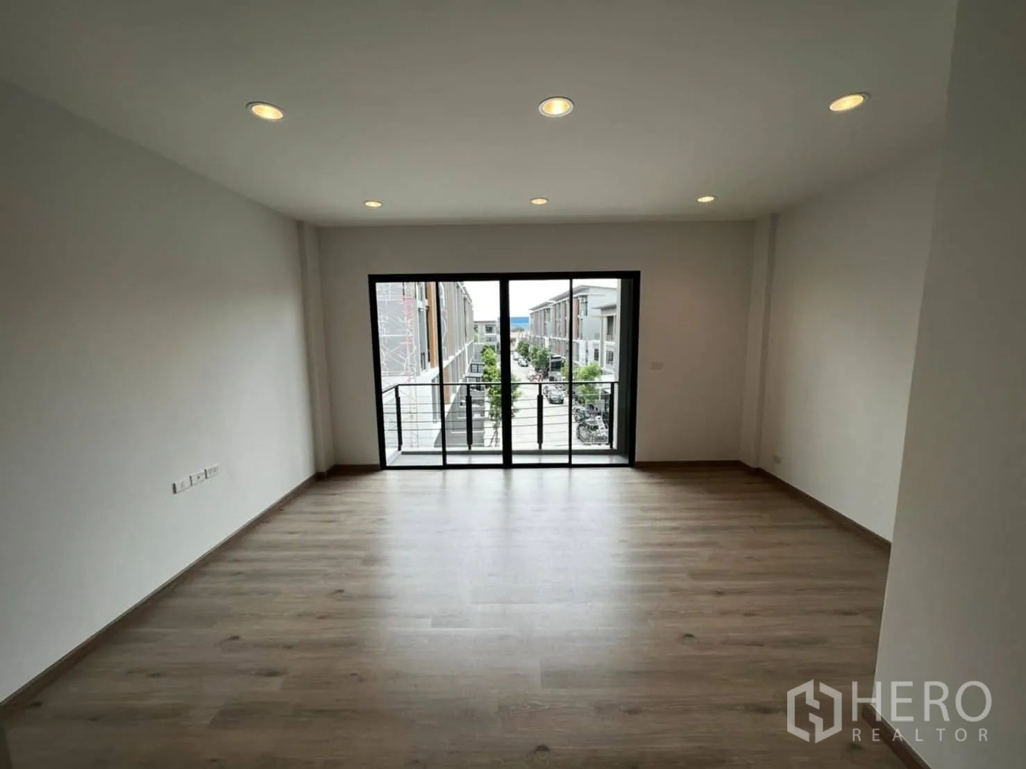 Townhouse for rent in Bang Khen, Bangkok - Spacious upper-floor room with wood flooring and balcony doors over the street.
