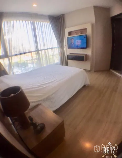 Condominium for rent in Sathon, Bangkok - Bedroom with built-in TV wall unit, large window draped with curtains and wood flooring.