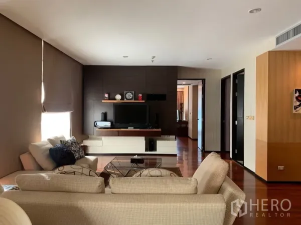 Condominium for rent - Lounge with L-shaped sofas facing a modern media wall and hallway to bedrooms.