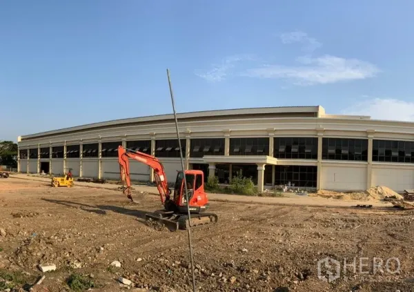 Warehouse for rent in Khlong Sam Wa, Bangkok - Modern two-storey warehouse exterior with wide glass frontage and open yard with excavator.