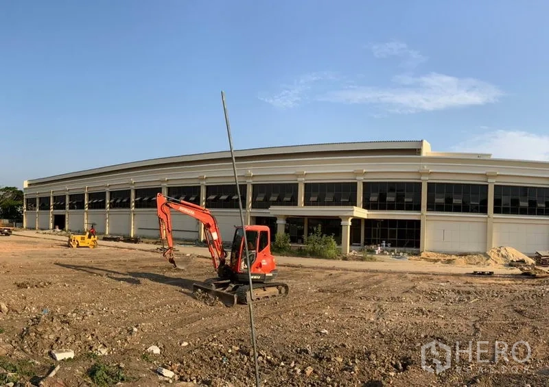 Warehouse for rent in Khlong Sam Wa, Bangkok - Modern two-storey warehouse exterior with wide glass frontage and open yard with excavator.