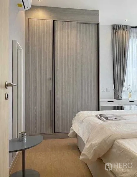 Condominium for rent in Watthana, Bangkok - Bedroom corner with built‑in wardrobe, bedside table and sheer curtains letting in natural light.