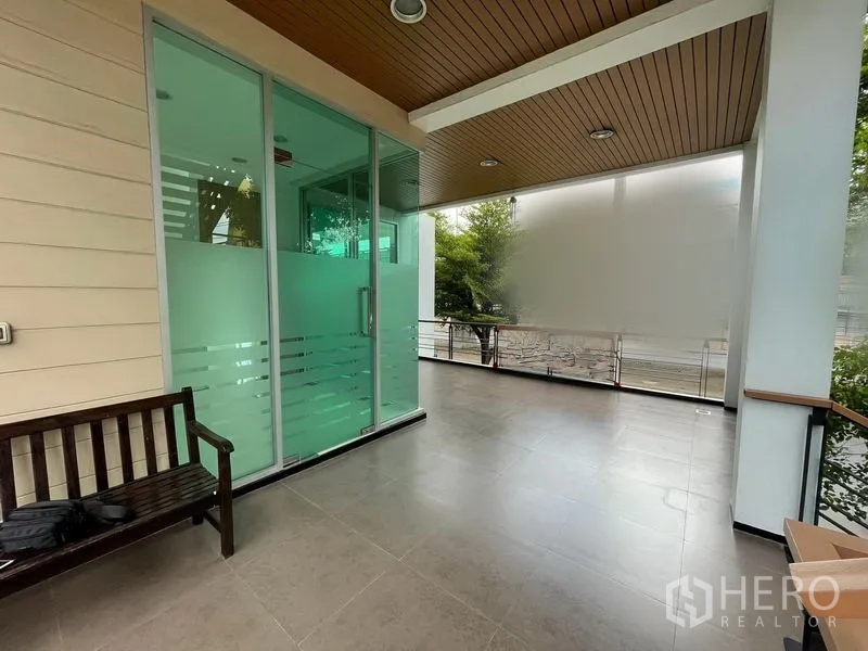 零售空间 出租在Bueng Kum, Bangkok - 阴凉阳台区，木长椅与磨砂玻璃入口，周围绿植。