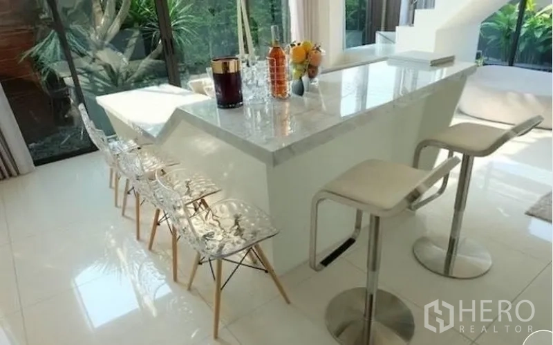 Townhouse for rent in Watthana, Bangkok - Marble breakfast bar with acrylic chairs beside full-height windows.