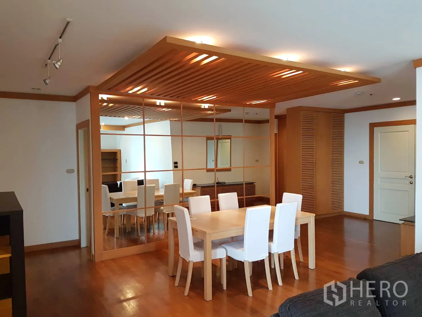 Condominium for rent in Pathum Wan, Bangkok - Open-plan living and dining room with wooden accents, track lighting and a full mirrored wall.