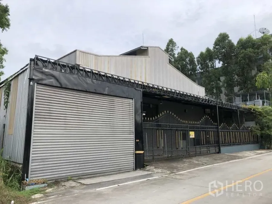 Warehouse for rent in Bang Phli, Samut Prakan - Street-facing warehouse exterior with a large roller shutter door and secure gated frontage.