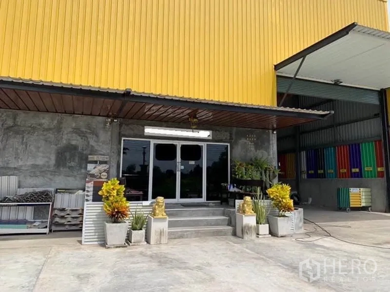 โรงงาน ขายในThanyaburi, Pathum Thani - ด้านหน้าโรงงานพร้อมทางเข้าออฟฟิศกระจก หลังคากันสาด และกระถางต้นไม้