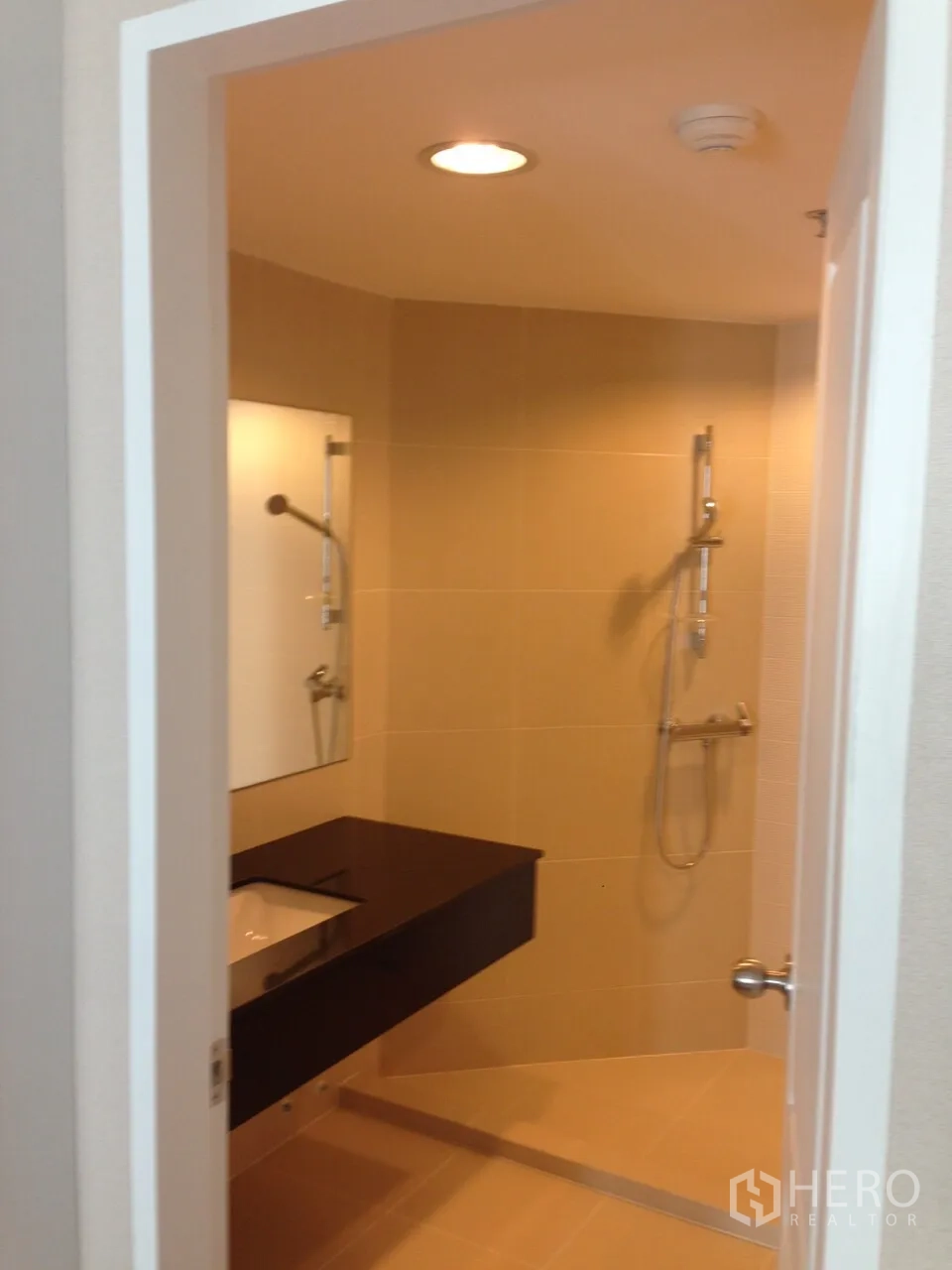 Condominium for rent in Huai Khwang, Bangkok - Modern bathroom featuring a walk-in shower, handheld shower set, mirror and dark floating vanity.