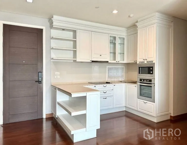 公寓 出租在Watthana, Bangkok - 白色L形厨房，内置烤箱、开放层架与中岛台面。