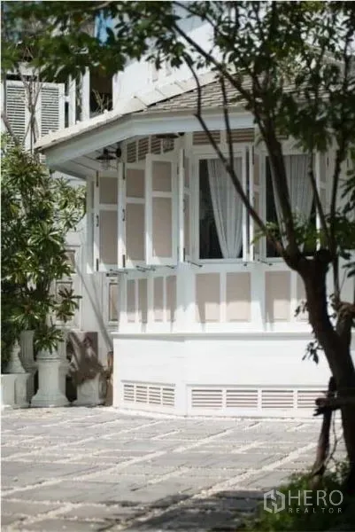 Detached House for rent in Bang Rak, Bangkok - Corner bay window of a white two-storey house with open shutters and a paved courtyard.