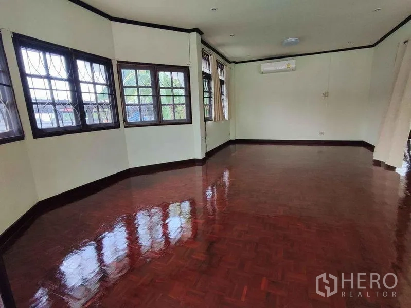Detached House for rent in Khlong Toei, Bangkok - Spacious living room with glossy parquet wood floors, multiple windows with security grilles and an air conditioner.