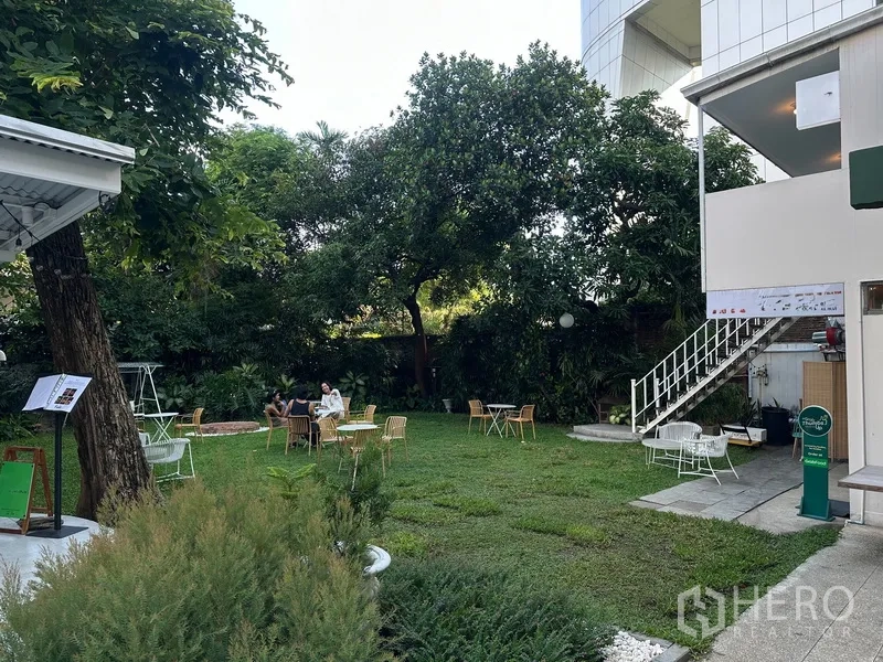 Retail Space for rent in Khlong Toei, Bangkok - Green garden courtyard with outdoor tables and chairs beside a staircase and building.