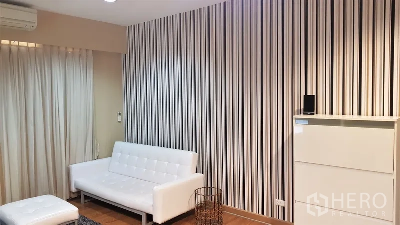 คอนโด ให้เช่าในRatchathewi, Bangkok - ห้องนั่งเล่นโทนอุ่น โซฟาสีขาว ผนังลายเส้นตั้ง พื้นไม้ และผ้าม่านทึบพร้อมไฟดาวน์ไลท์