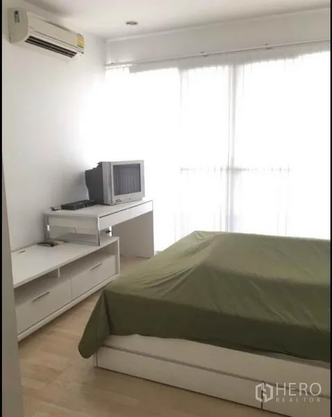 Townhouse for sale in Khlong Toei, Bangkok - Cozy bedroom with green bedspread, desk, small TV and floor-to-ceiling window.