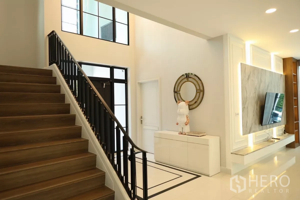 Detached House for rent or sale in Saphan Sung, Bangkok - Entrance hall and staircase with black handrail beside a sleek TV wall.