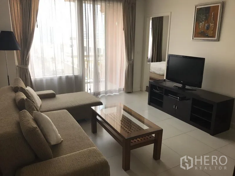 Condominium for rent in Bang Rak, Bangkok - Bright living room with L‑shaped sofa, TV console, glass coffee table and balcony windows in a Bang Rak condo.
